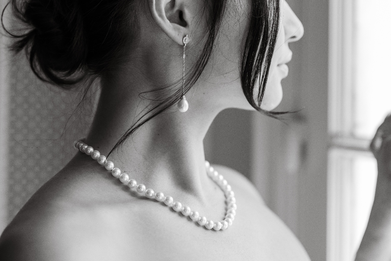 A close-up of a bride wearing an ornate floral necklace in a calm outdoor setting.