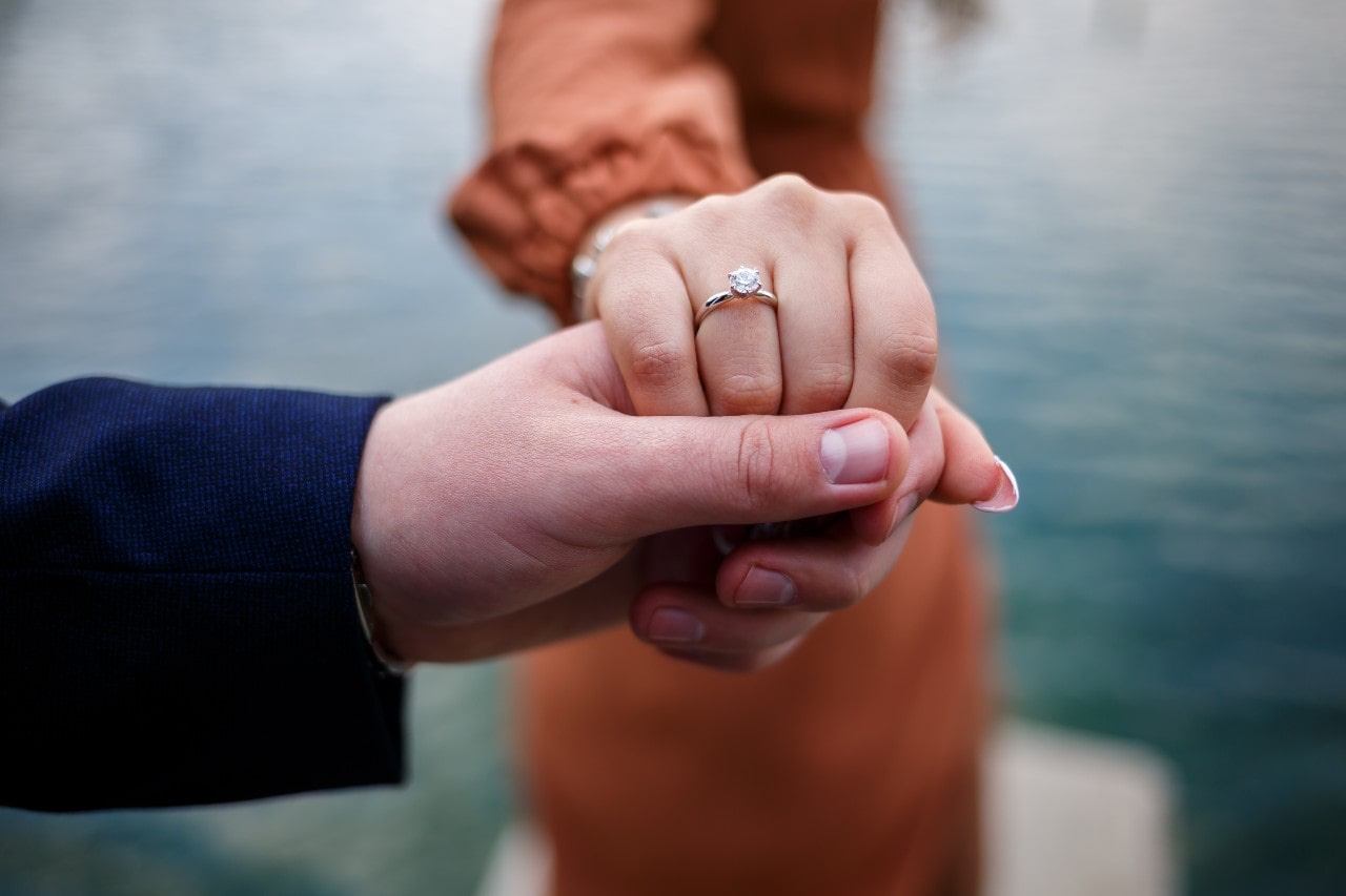 A man holding the hand of a woman wearing an engagement ring