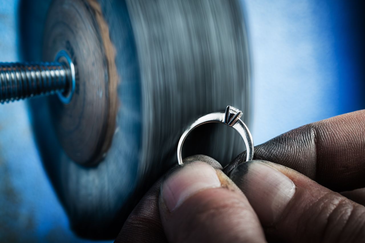 a man’s fingers holding up an engagement ring to a buffering machine