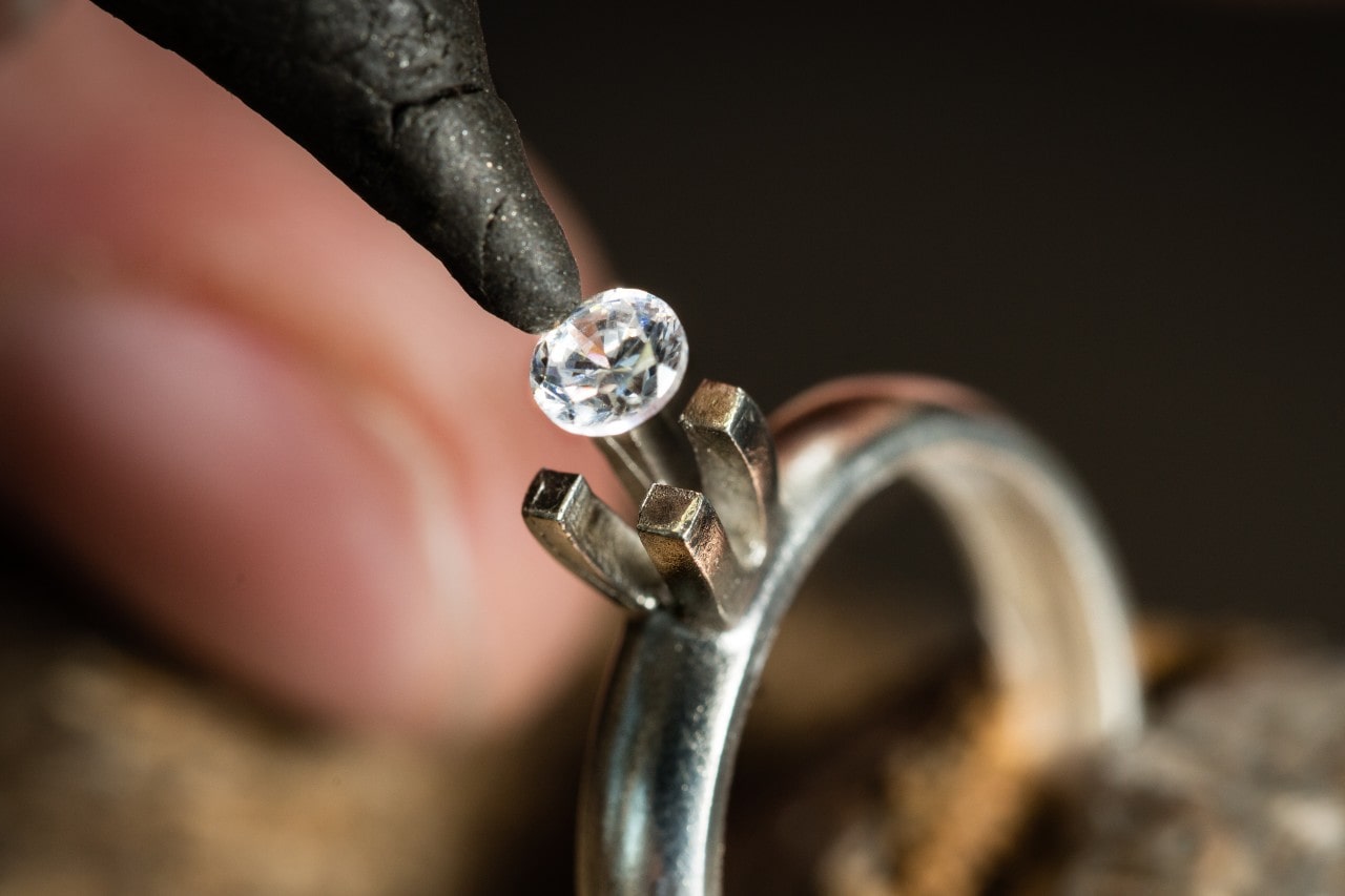 close up image of a round cut diamond being placed into a prong setting engagement ring