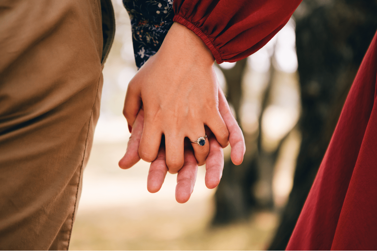 A couple holding hands outdoors in the fall, the woman wearing a sapphire engagement ring.