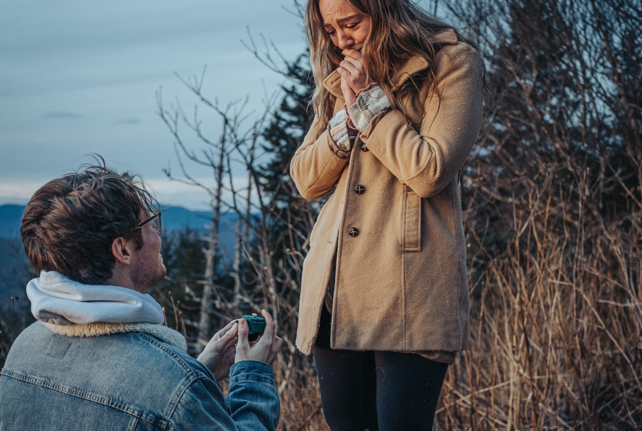 A man kneeling and presenting a ring box to his partner during the holiday season.