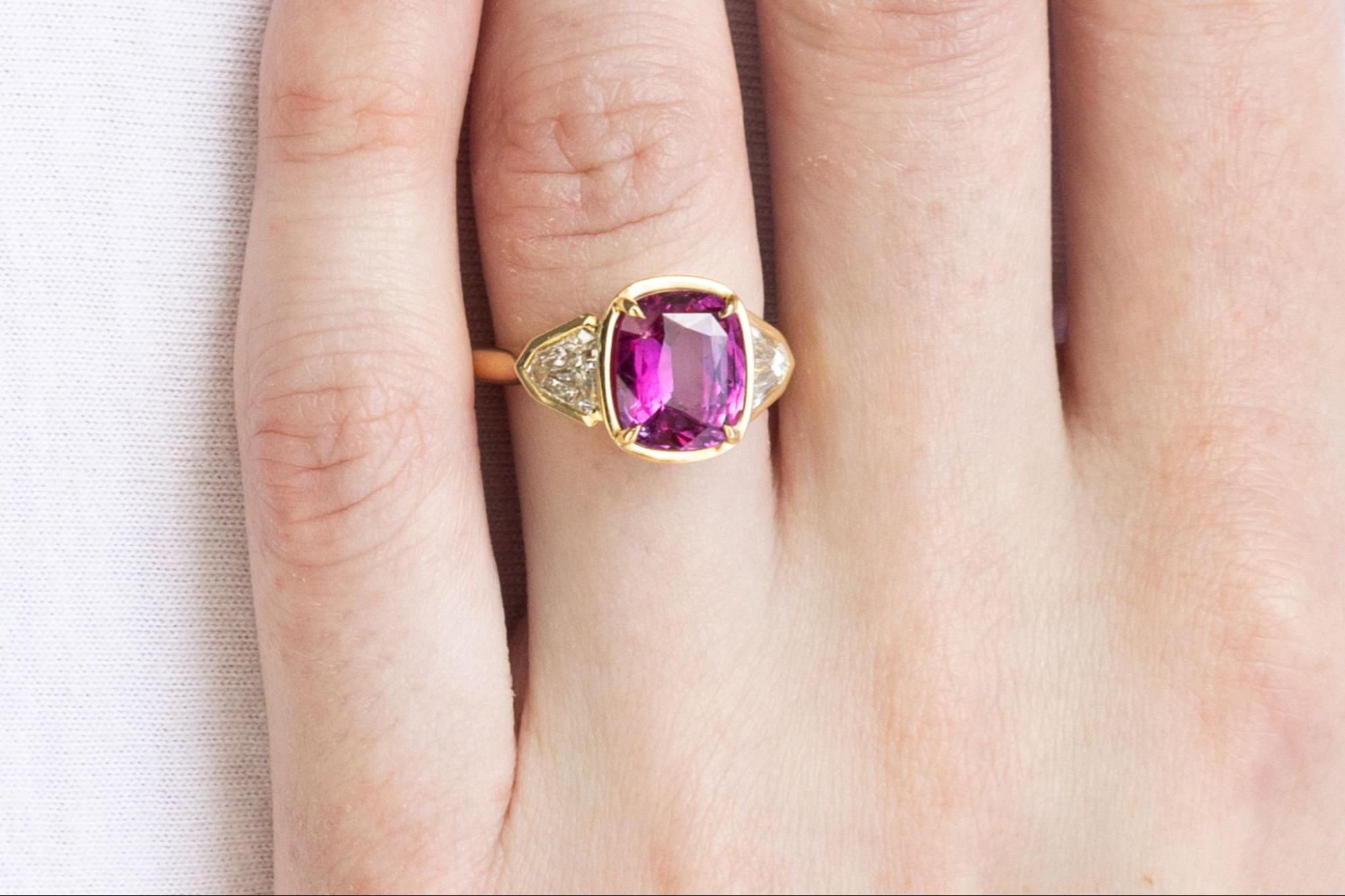 A yellow gold three stone ruby ring with a gorgeous pink-red cushion cut ruby and two triangular radiant diamonds on each side.