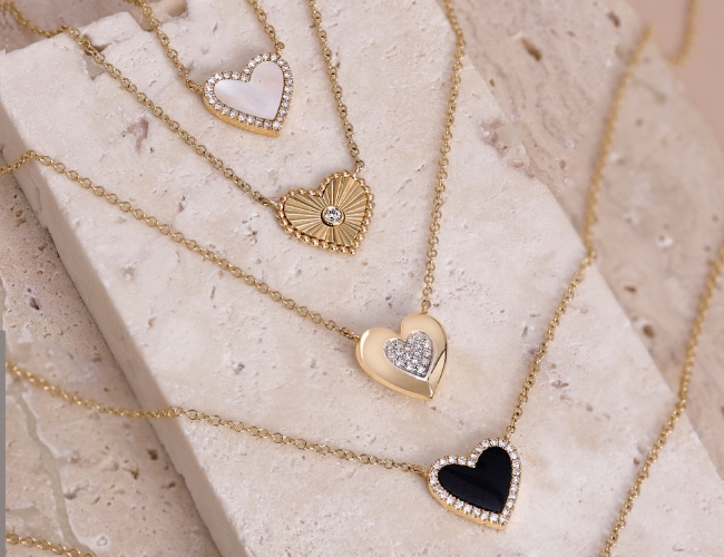 Four heart shape gold necklaces with different details; from top down, diamond halo and mother of pearl in-lay, textured heart burst with bezel-set round diamond in the center, yellow gold halo and pavé-set diamond center heart, and a diamond halo and black jade in-lay.