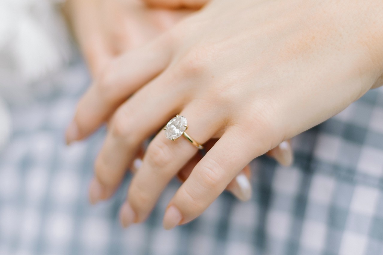 A woman’s hands, one of which is adorned with a yellow gold solitaire engagement ring.