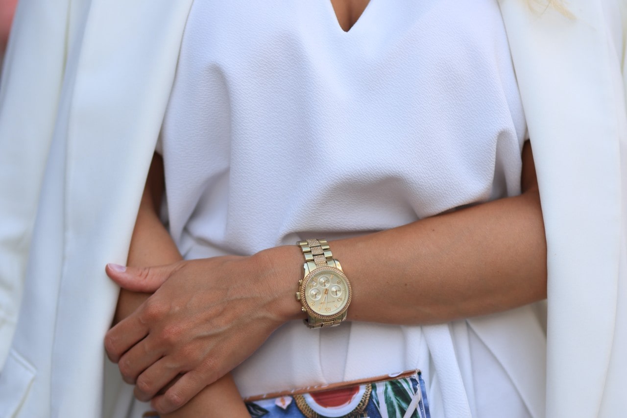 Woman in stylish white outfit and colorful clutch wearing a gold watch