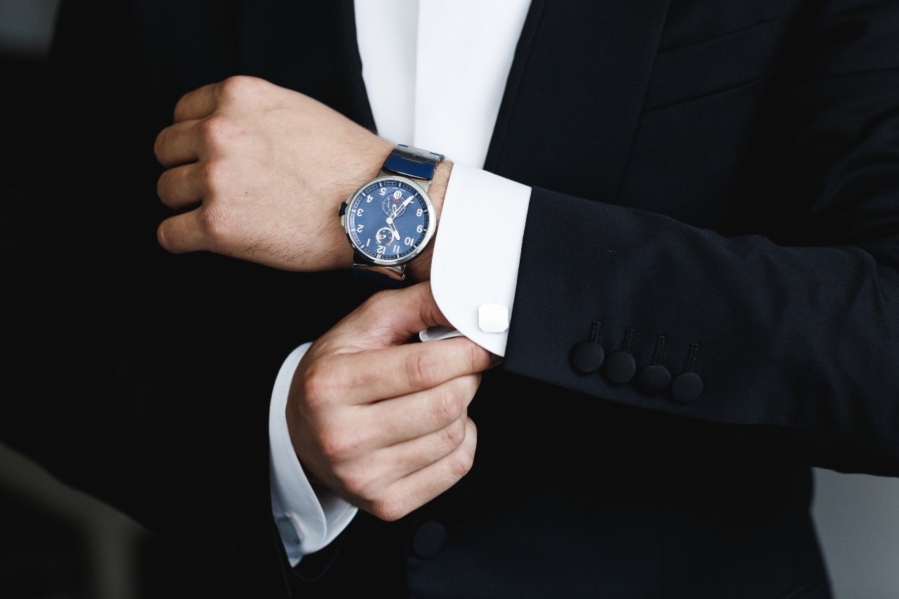 Man in a dark suit wearing a blue dial and leather strap watch as a pop of color with accessories