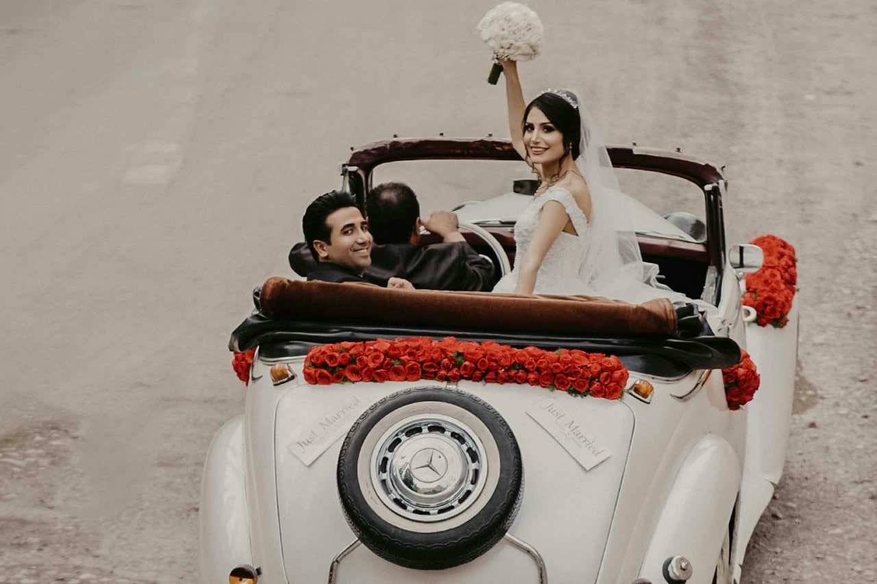 a bride and groom in the back of a convertible leaving their wedding