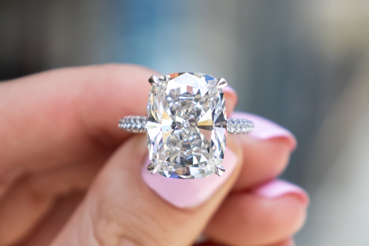 a cushion cut engagement ring with side stones being held in the fingers of a woman