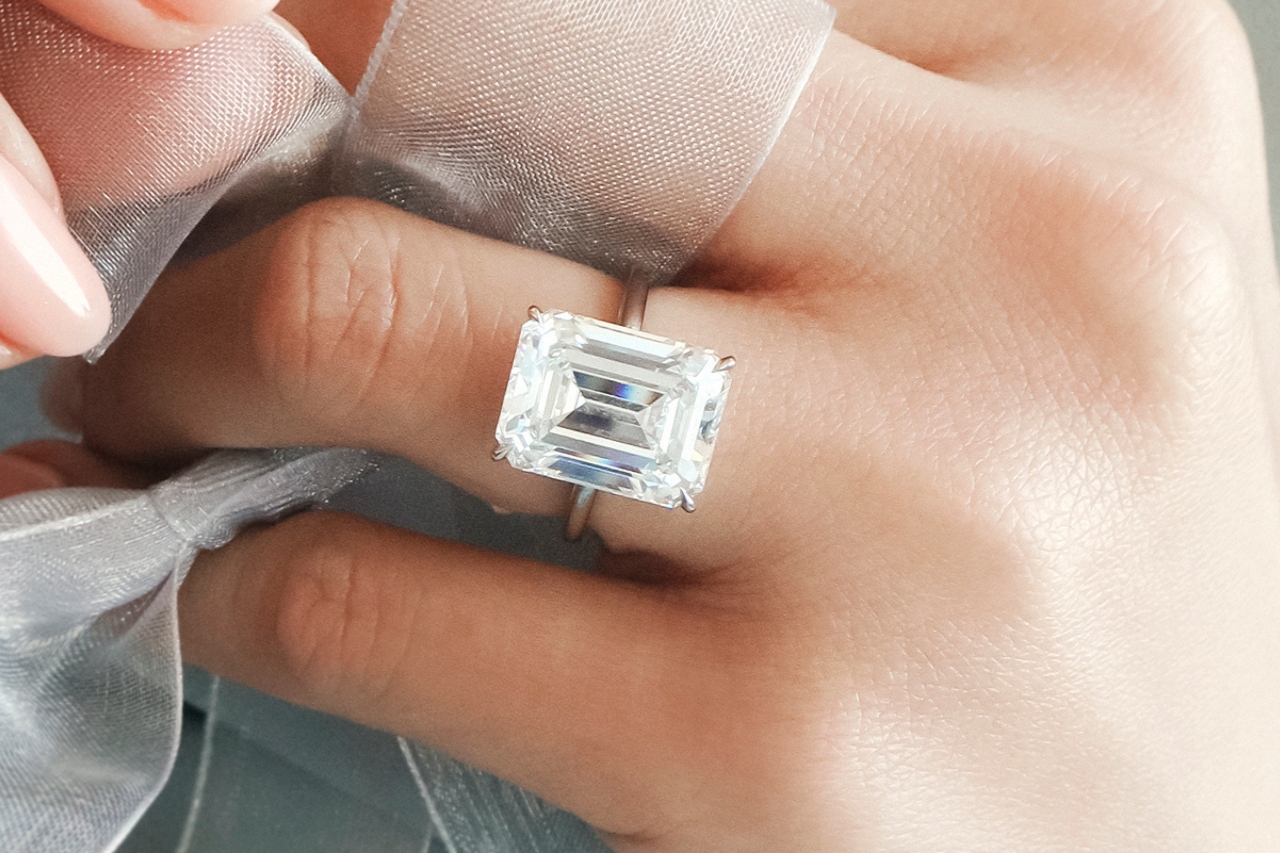 a woman with an emerald solitaire engagement rings with a chiffon ribbon interlaced through her hands