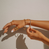 A women's wrist is outstretched showcasing a hand stacked with beautiful gold and diamond bracelets and gold rings. 