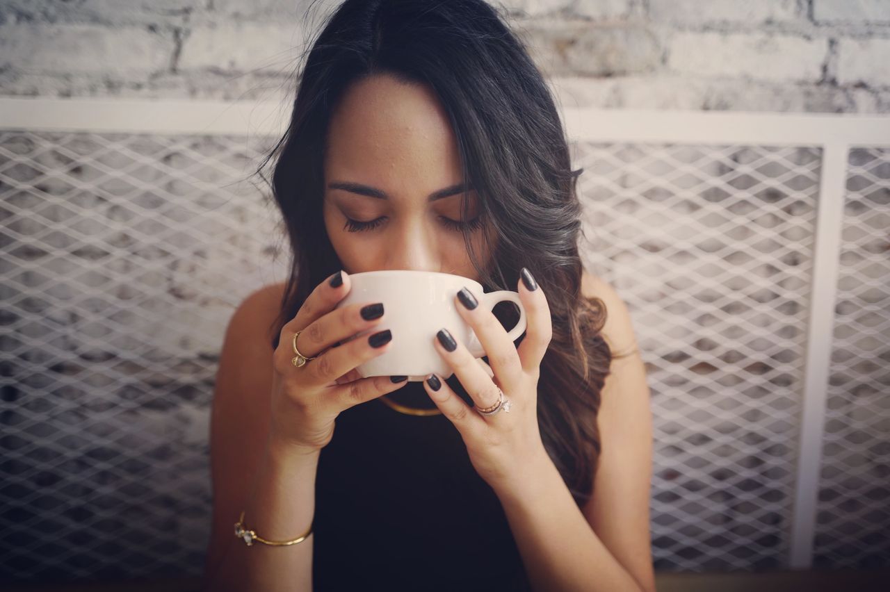 A casually dressed young woman wearing multiple rings sipping coffee.