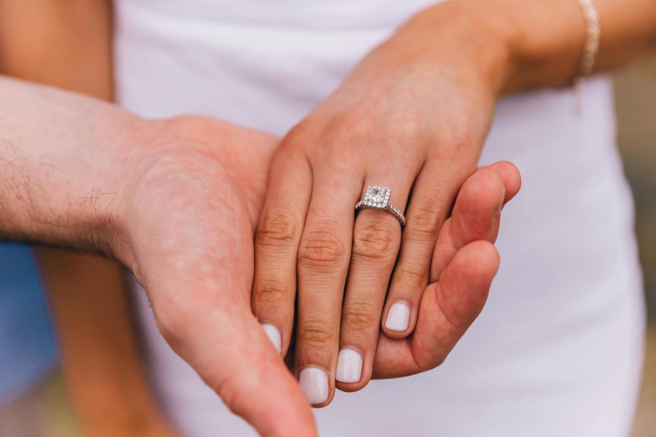 A close-up of a bride-to-be’s hand in her groom’s, a halo engagement ring on her finger.