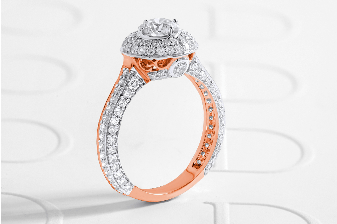 A close-up of an opulent two-tone halo engagement ring on a white backdrop.