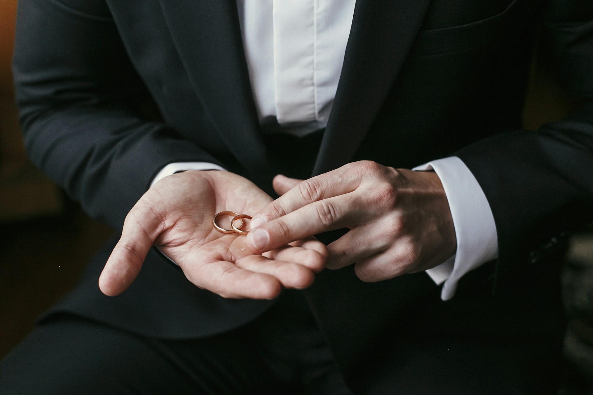 A groom holding two yellow gold wedding bands in his hands.