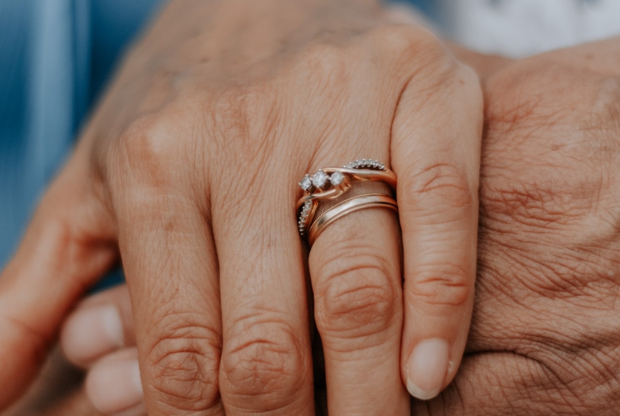 A close-up image of a woman’s hand adorned with a rose gold wedding band and engagement ring.