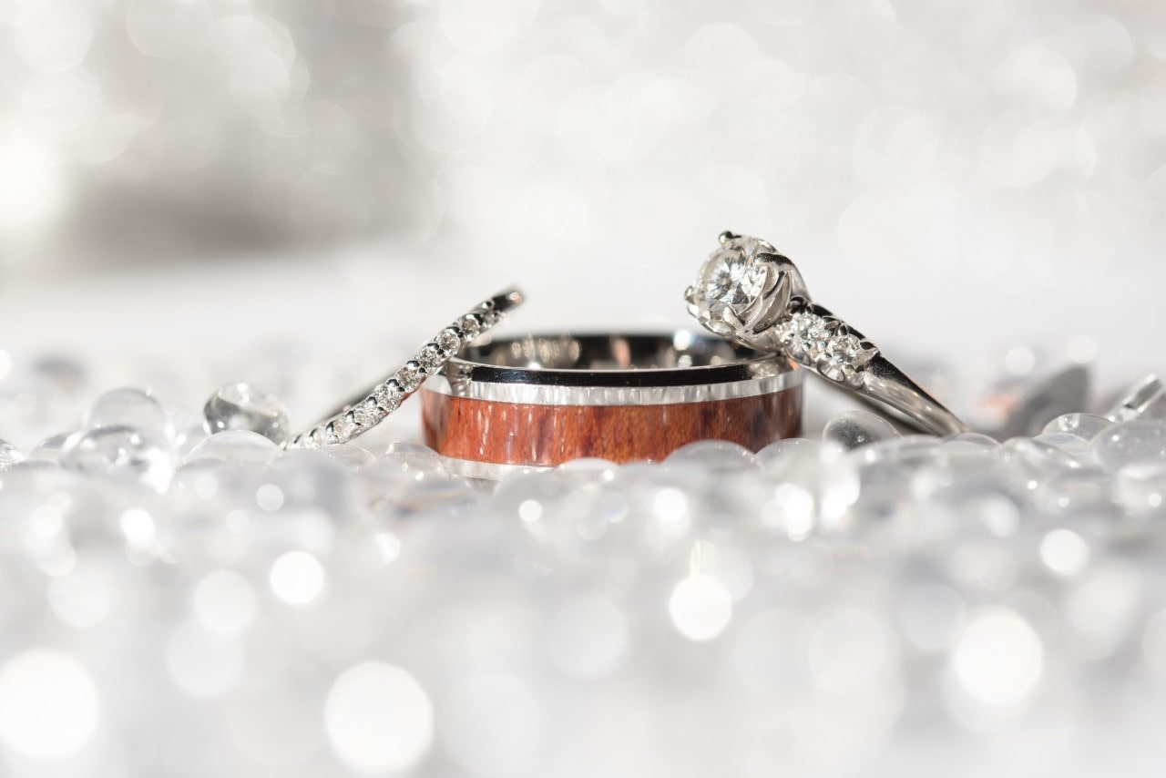 A white gold wedding band and engagement ring displayed atop a white gold men’s wedding band.