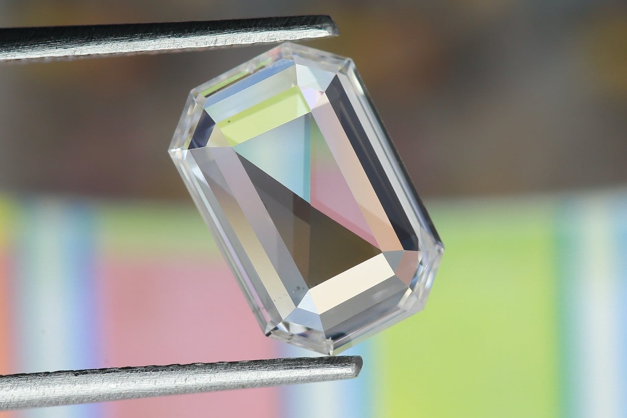 A close-up of an emerald-cut diamond carefully held by jeweler’s tweezers.